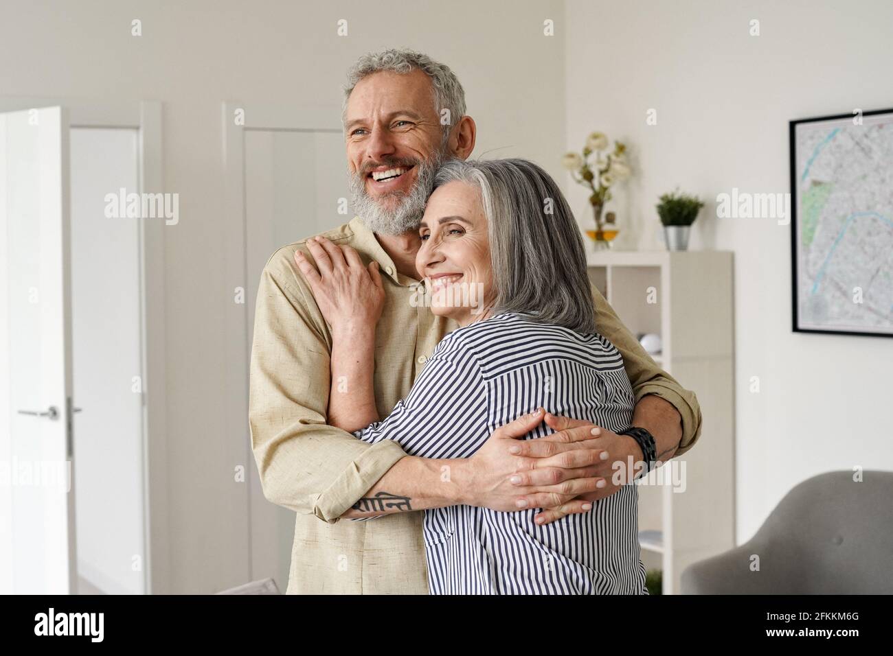 Glückliches reifes Paar umarmt, wegschaut, denkt, träumt von der Zukunft zu Hause. Stockfoto