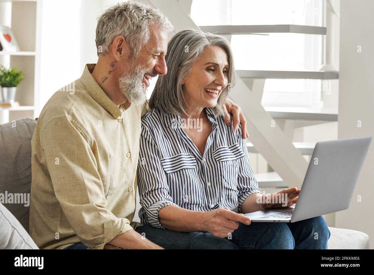 Ein glückliches, älteres Paar im mittleren Alter, das einen Laptop benutzt und einen Computer auf der Couch ansieht. Stockfoto