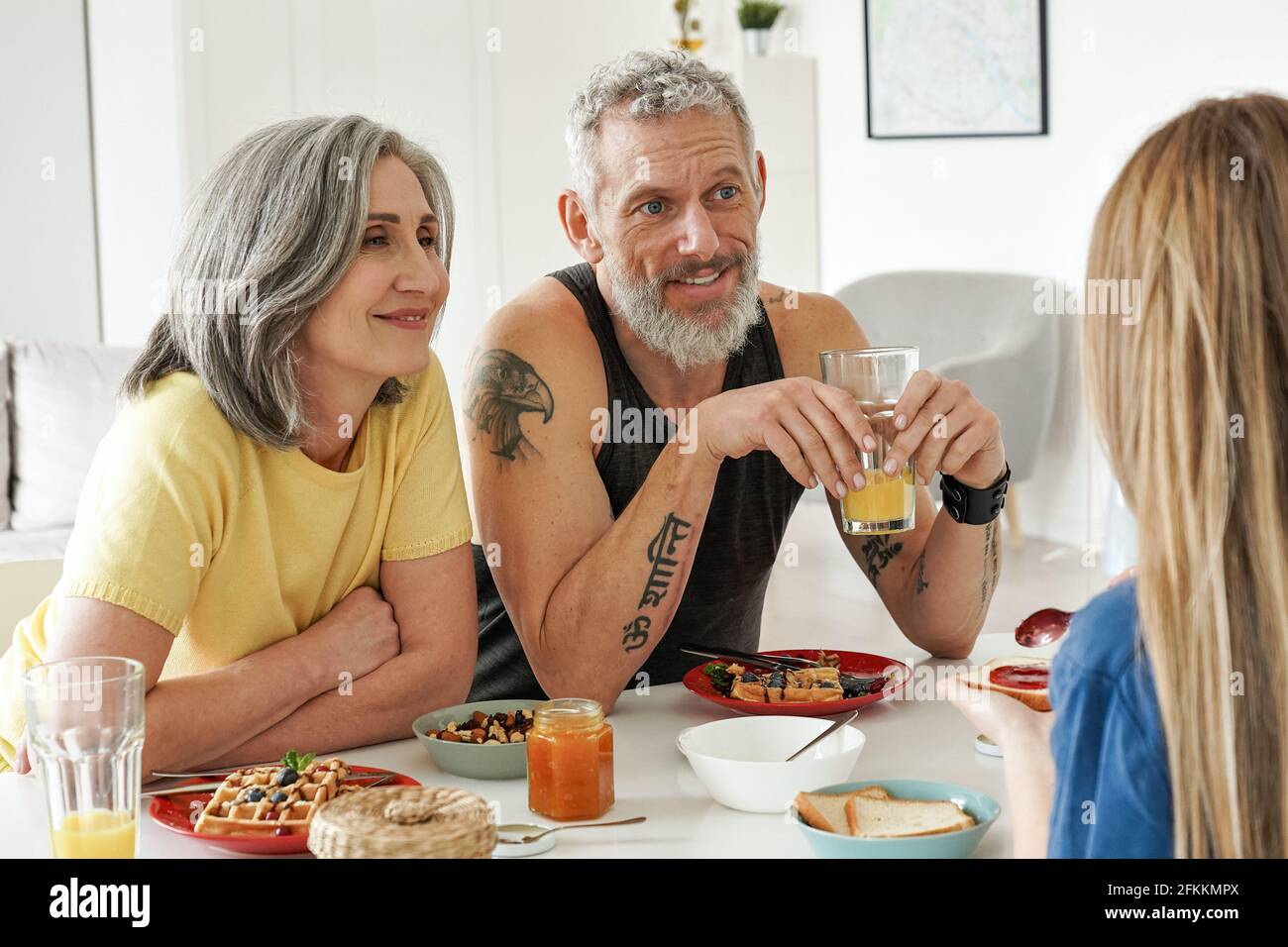 Glückliches älteres Familienpaar beim Frühstück mit Tochter sitzen am Küchentisch. Stockfoto
