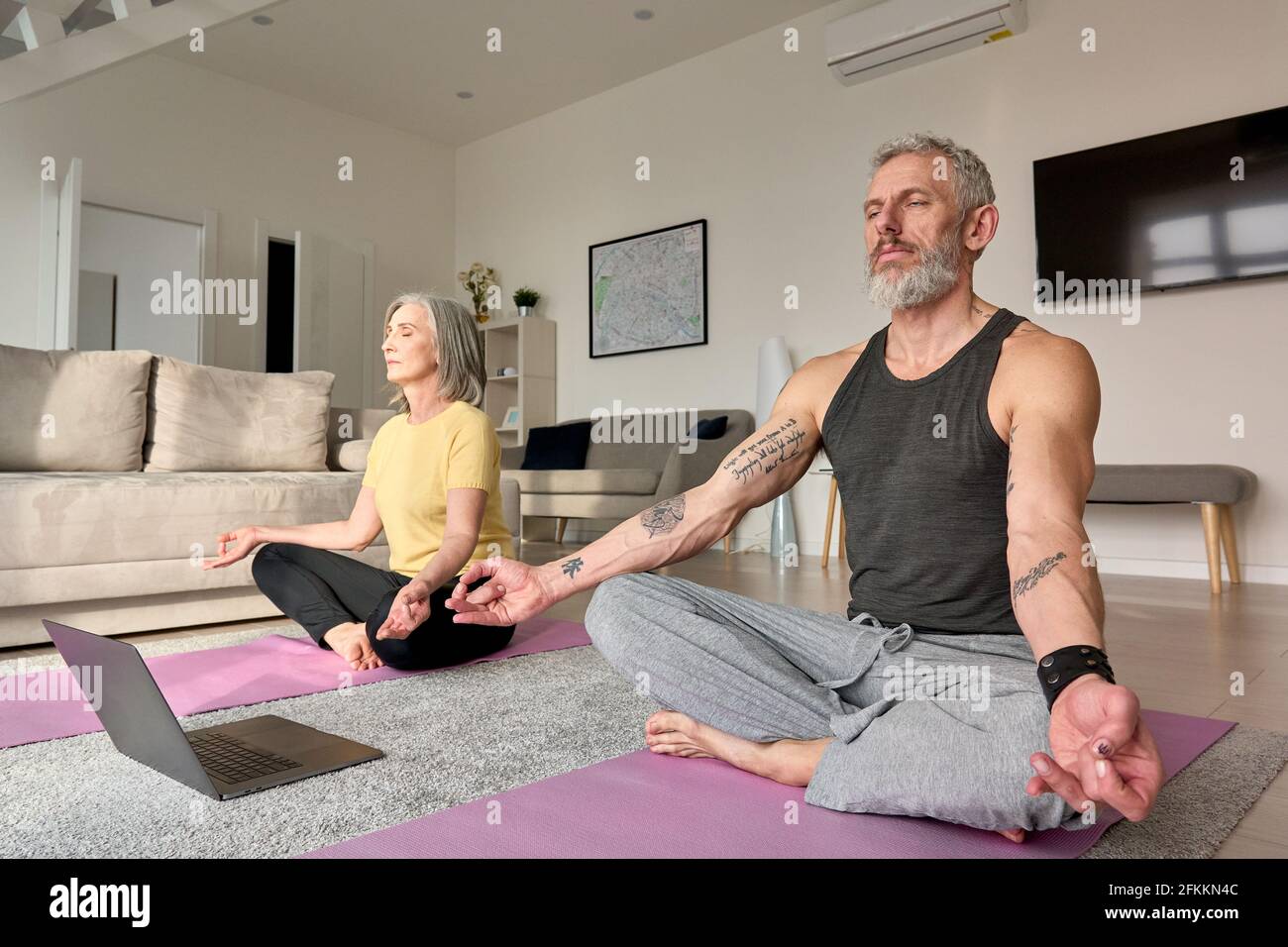 Seniorehepaar meditiert dabei virtuelle Yoga-Posen beobachten Online-Kurs zu Hause. Stockfoto