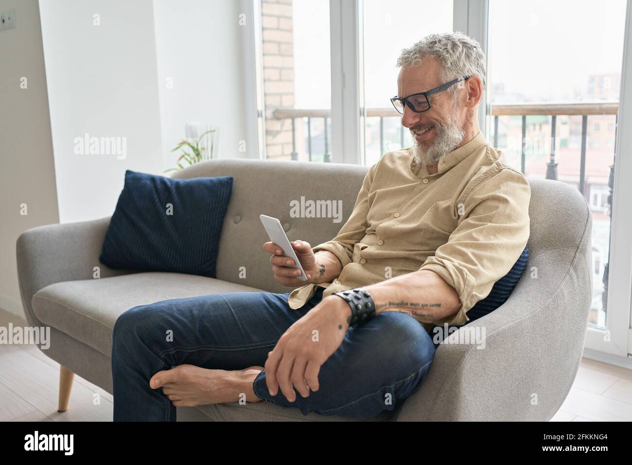 Ein glücklicher älterer Mann mittleren Alters, der mit dem Telefon telefoniert und zu Hause auf der Couch sitzt. Stockfoto