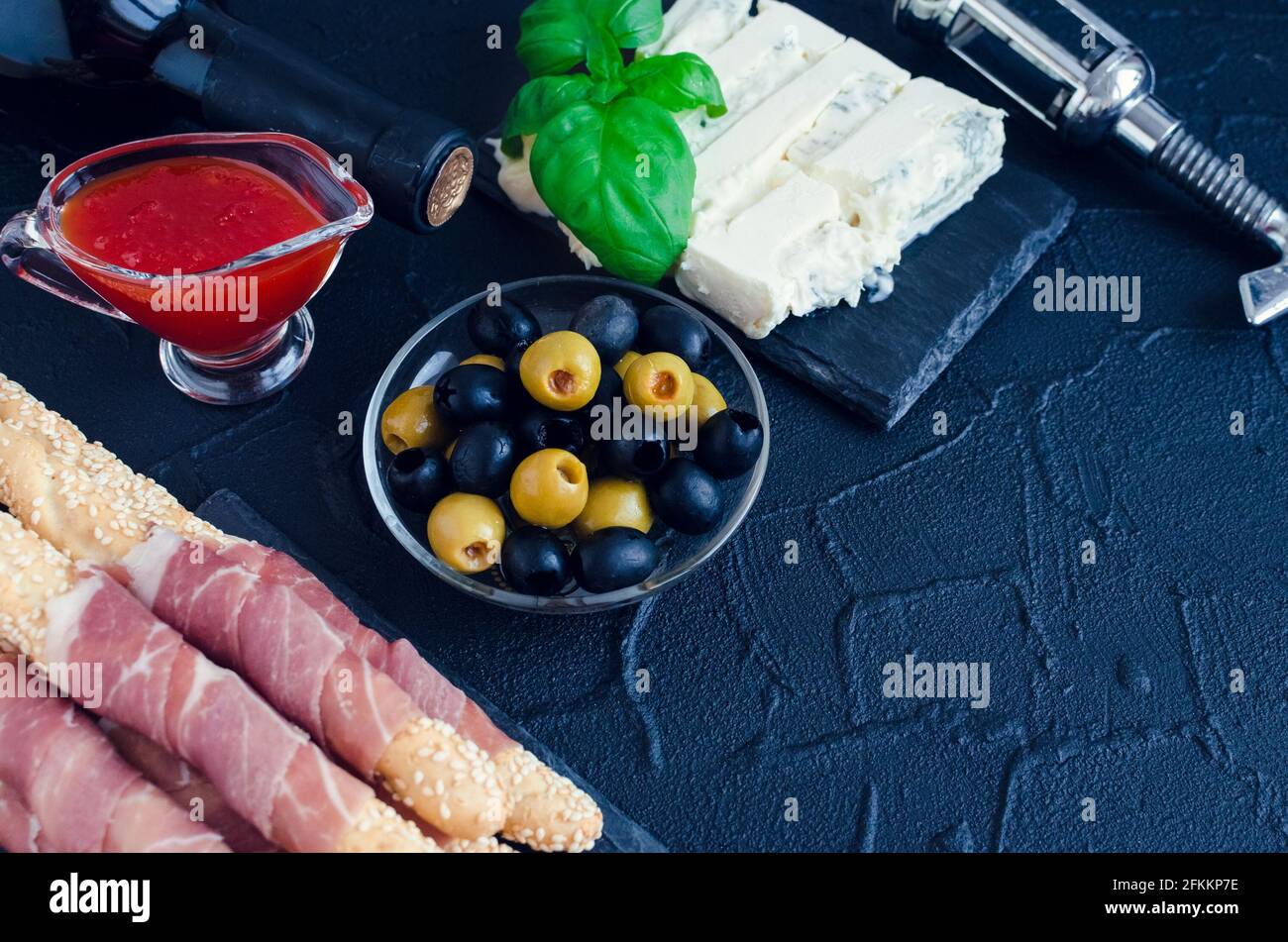 Flasche Wein mit Antipasti auf dunklem Stein Hintergrund. Grissini Grissini mit Schinken, Basilikum, Oliven, Gorgonzola und Chili ja Stockfoto