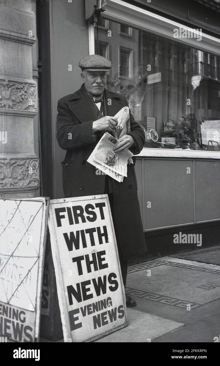 1950, historisch, ein älterer männlicher Zeitungsverkäufer, in Mantel und Stoffkappe, der draußen auf einem Bürgersteig stand, der die Evening News verkauft, London, England, Großbritannien. Stockfoto