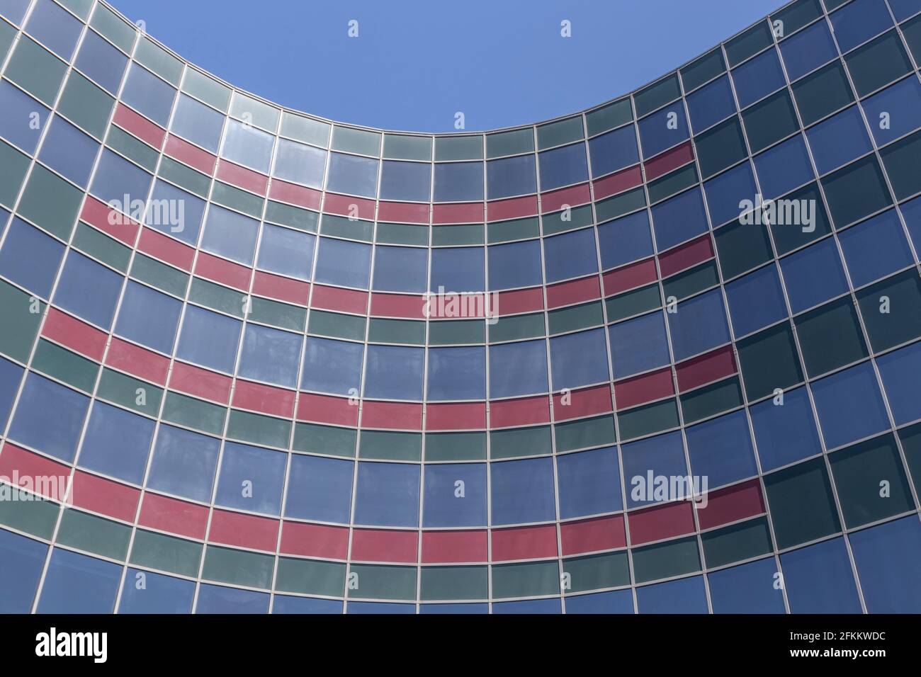 Geschwungene geometrische Architektur. Blaues Gebäude mit roten und grünen Fenstern vor blauem Himmel. Stockfoto
