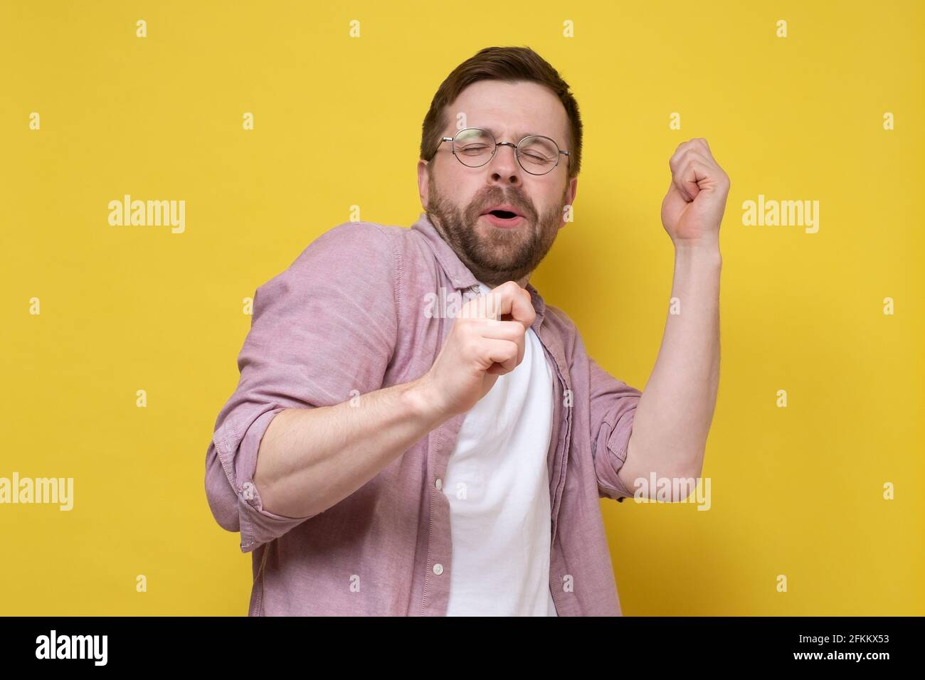 Kaukasischer Mann in guter Laune, tanzt er Bewegungen mit den Händen und singt mit geschlossenen Augen. Gelber Hintergrund. Stockfoto