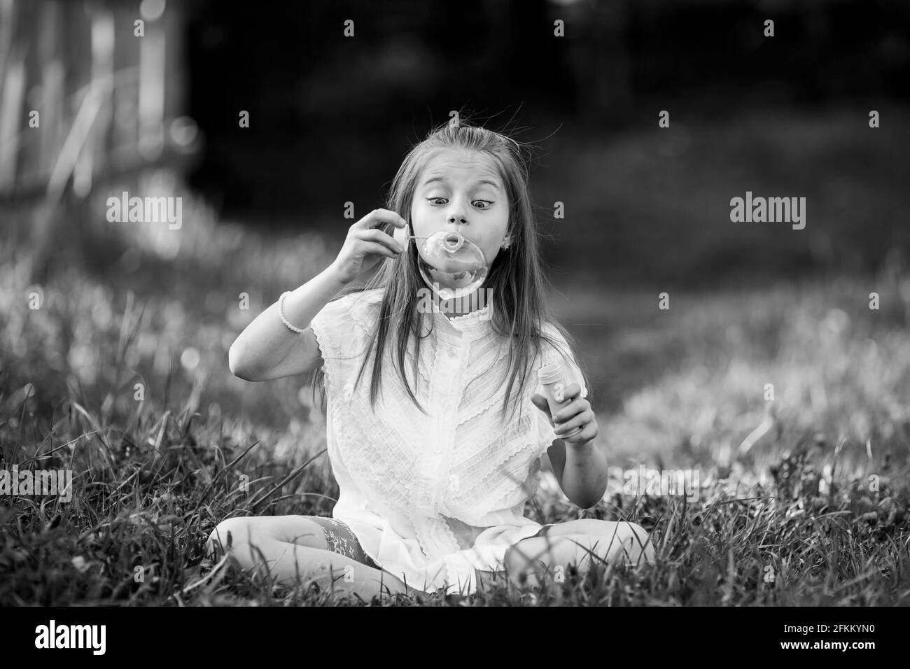 Ein kleines Mädchen bläst im Freien emotional Seifenblasen auf. Schwarzweiß-Foto. Stockfoto