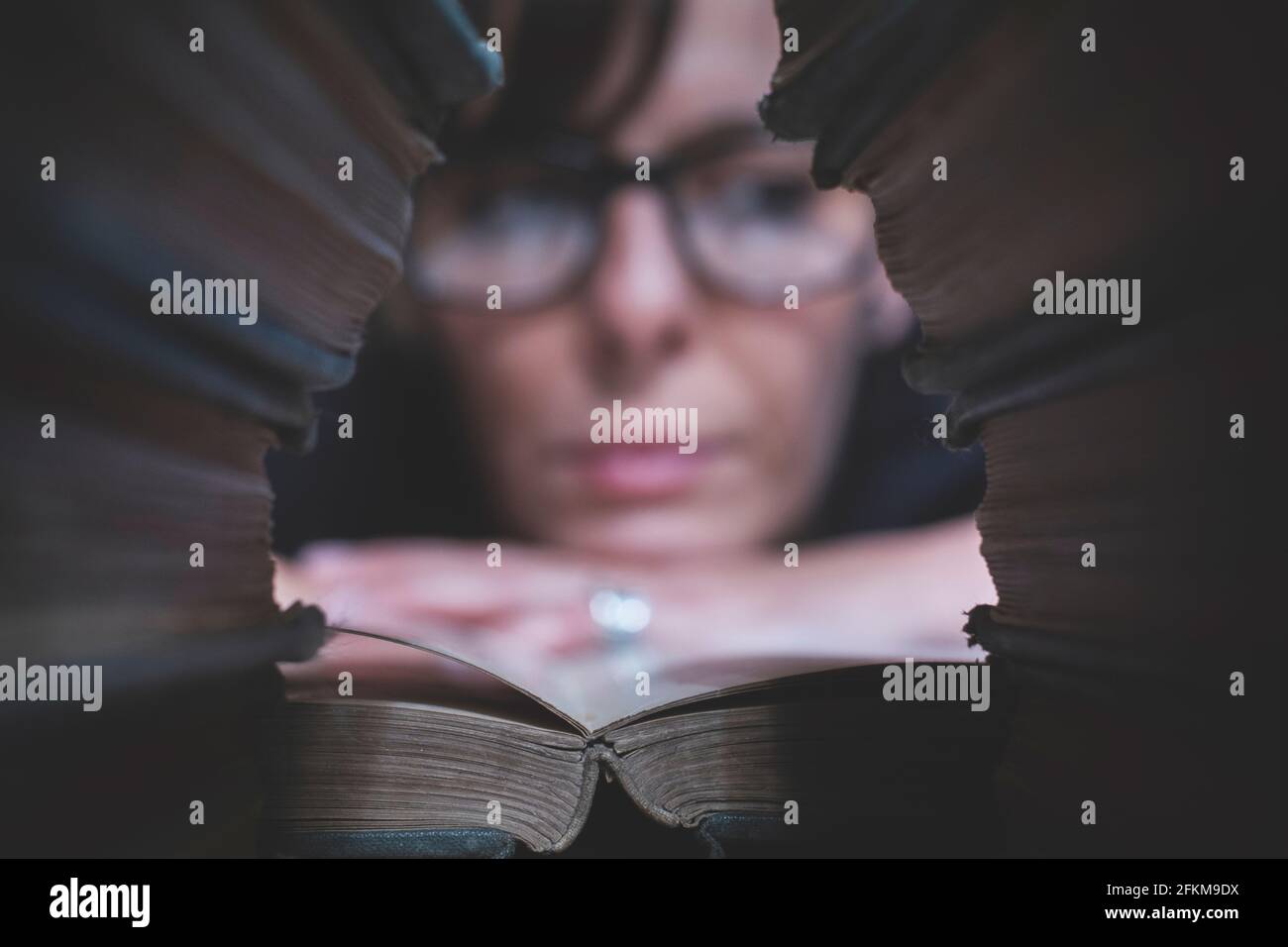 Eine Frau mit vielen Büchern liest bequem in ihrer Bibliothek Stockfoto