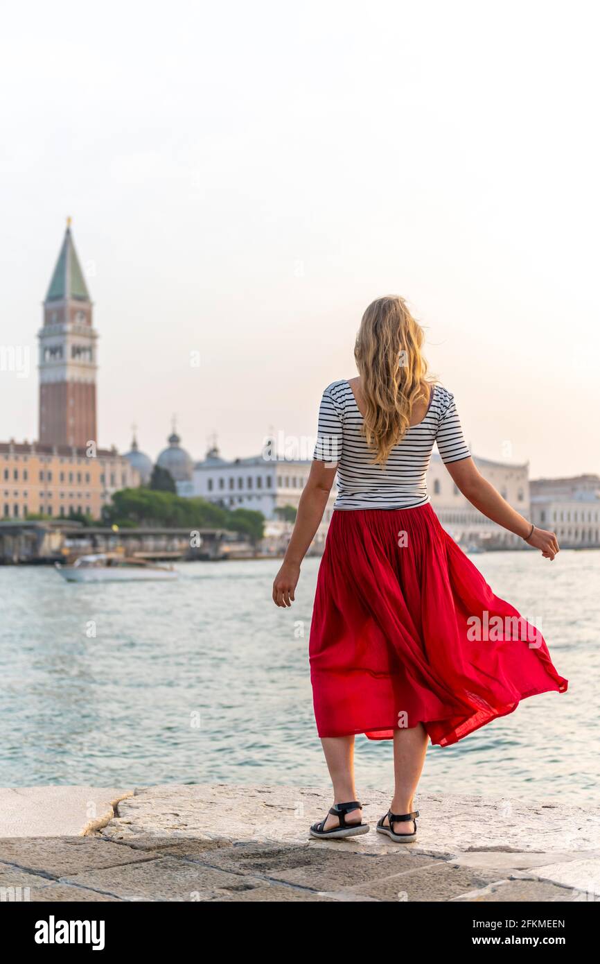 Junge Frau mit rotem Rock am Wasser, Blick auf Venedig und den Glockenturm Campanile, Venedig, Venetien, Italien Stockfoto