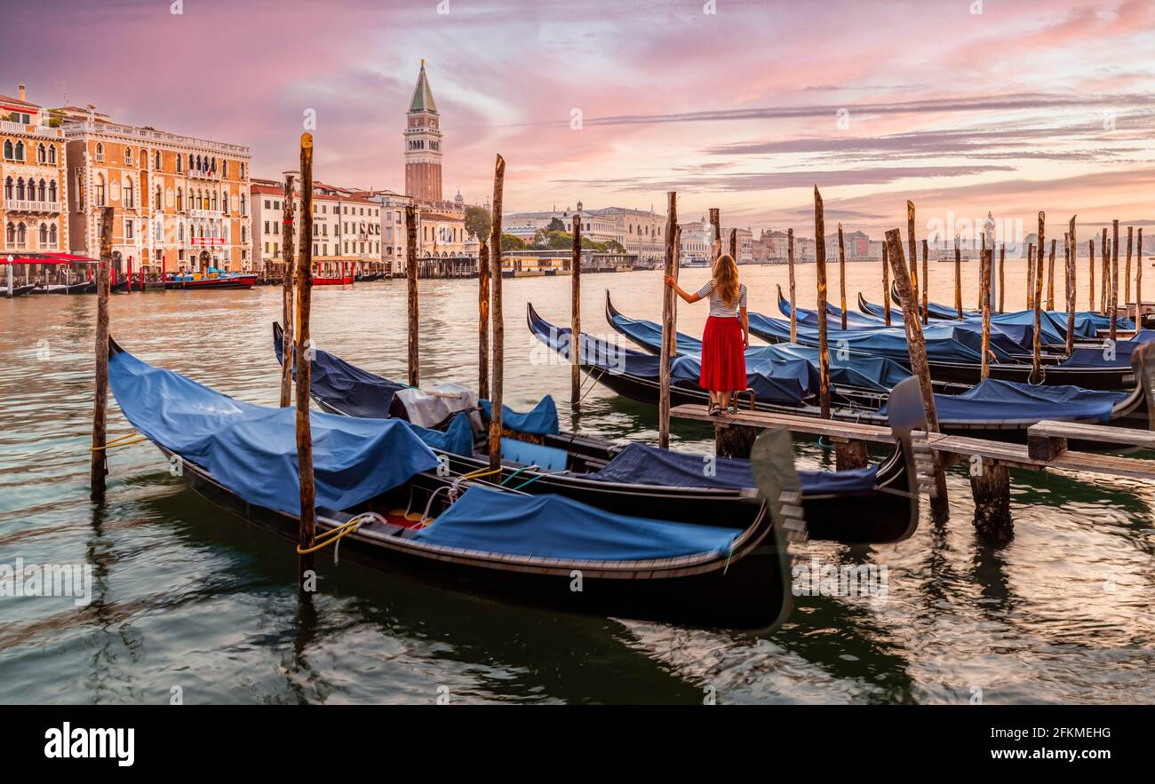 Frau mit rotem Kleid und Blick auf Venedig, Abendstimmung, Sonnenuntergang am Canale Grande, Gondeln am Pier, Campanile-Glockenturm, Venedig, Region Venetien Stockfoto