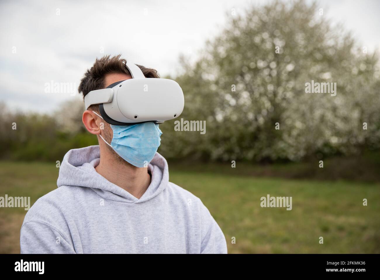 Ein Mann benutzt draußen ein Virtual-Reality-Headset, das eine OP-Maske trägt Stockfoto