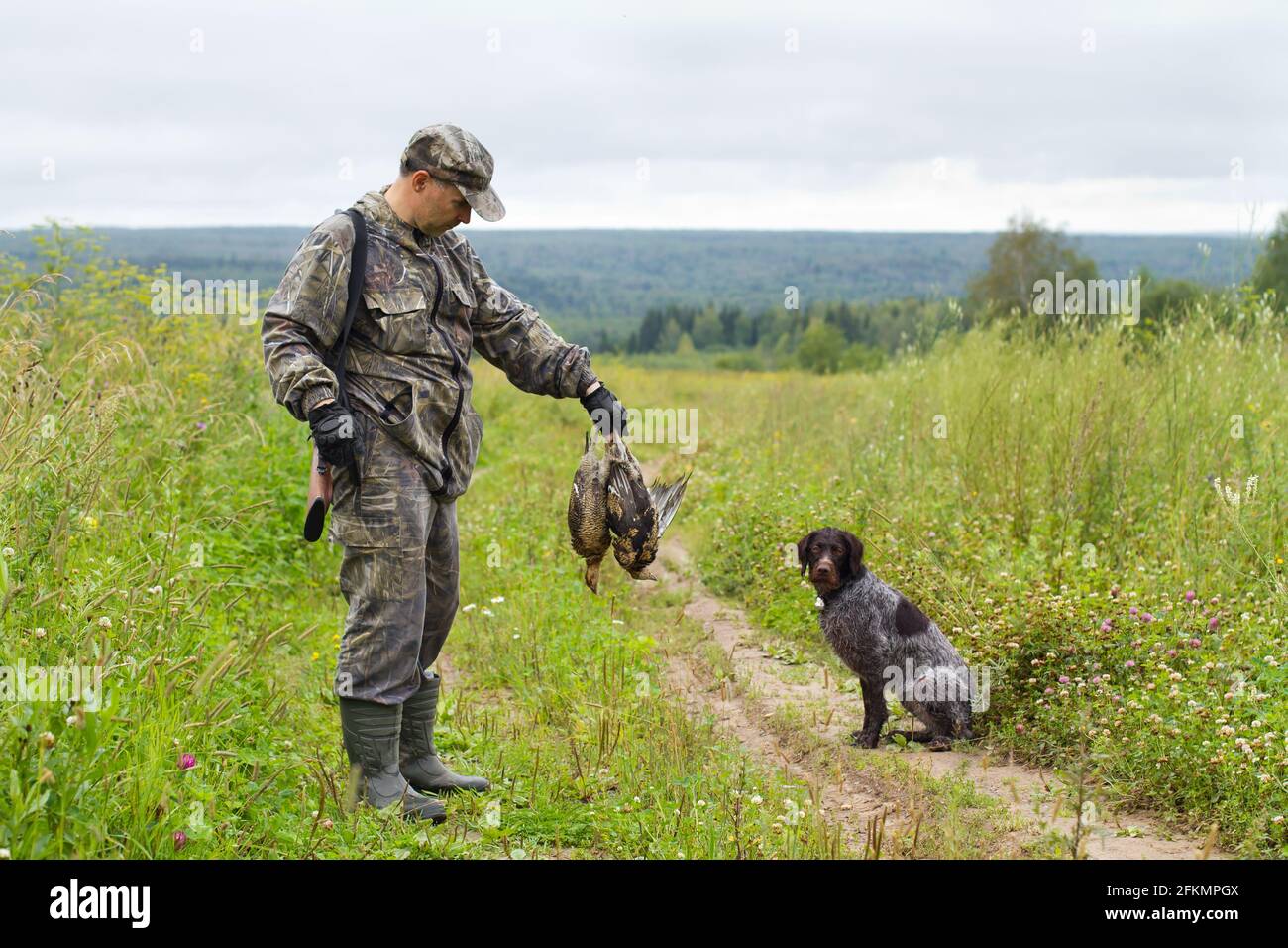 hunter mit seinem Schützenhund ist auf der Feldstraße mit Beute in der Hand Stockfoto
