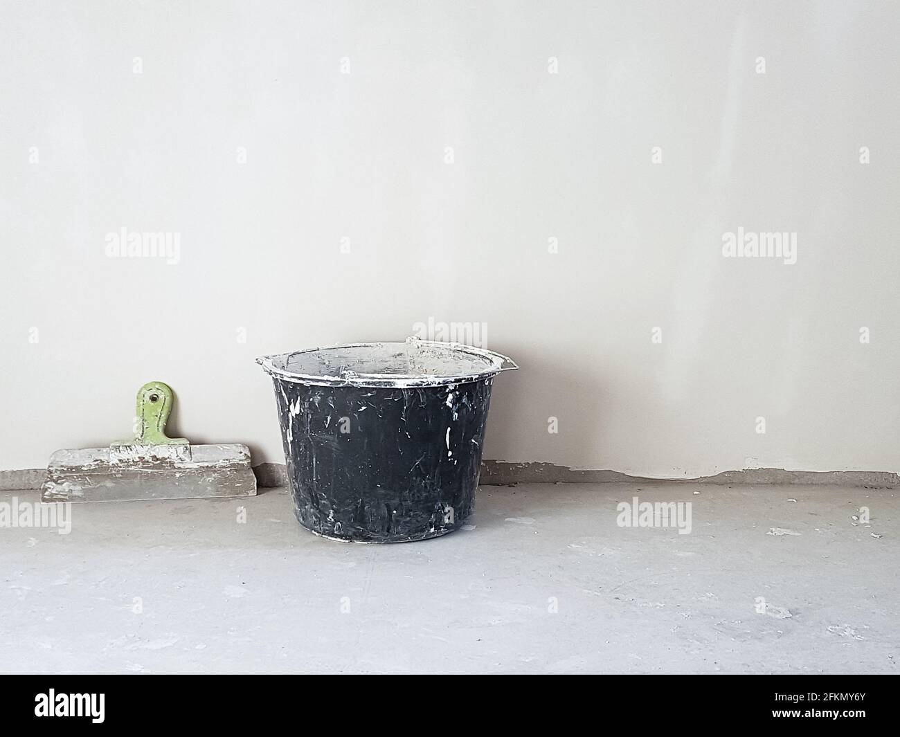 Kitt Messer und Eimer in leerem Raum an der Wand auf Zementboden. Innenhintergrund des Zimmers. Stockfoto