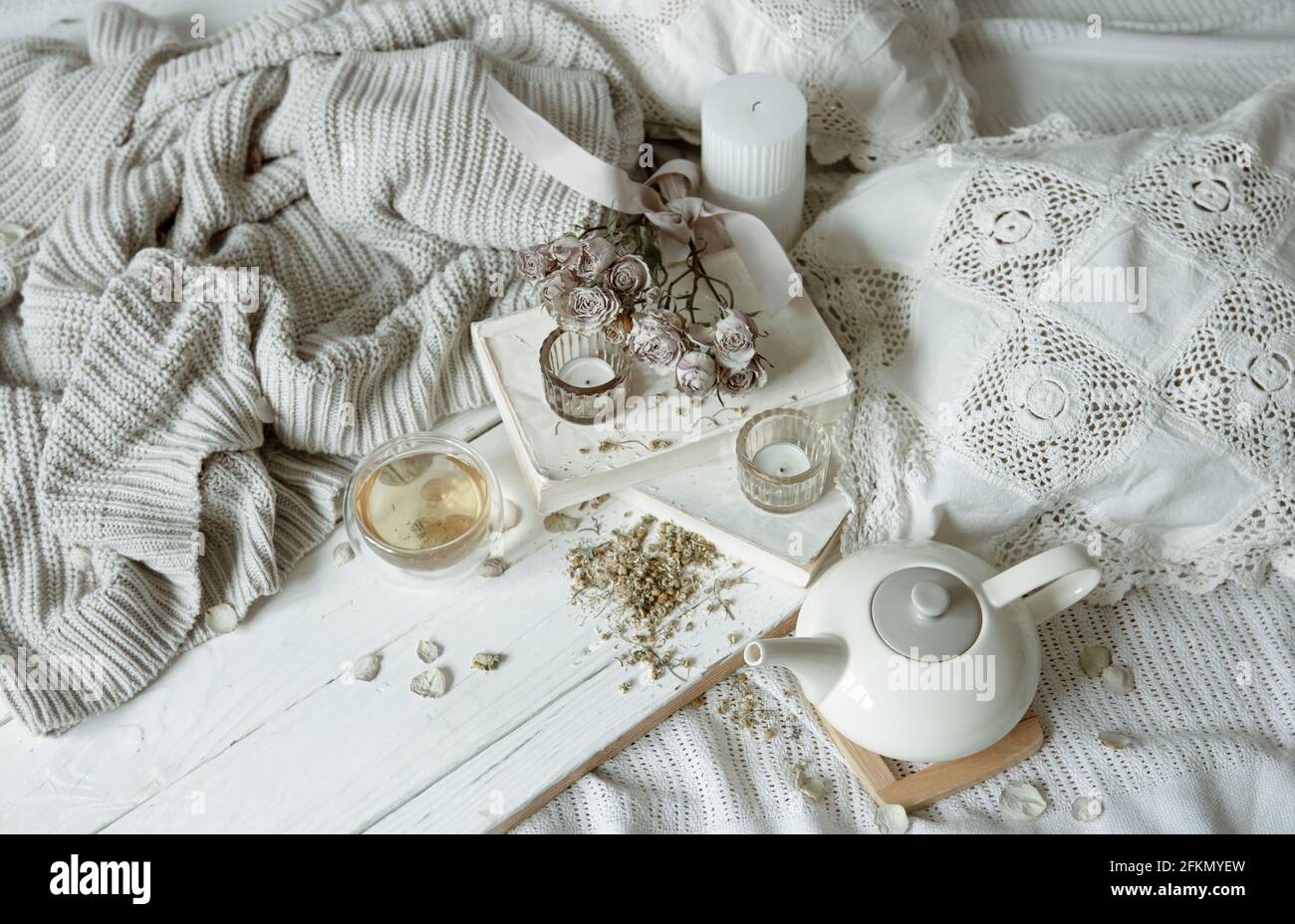Gemütliches Licht Stillleben mit Kerzen, Tee, Teekannen und Blumen als Dekor. Stockfoto