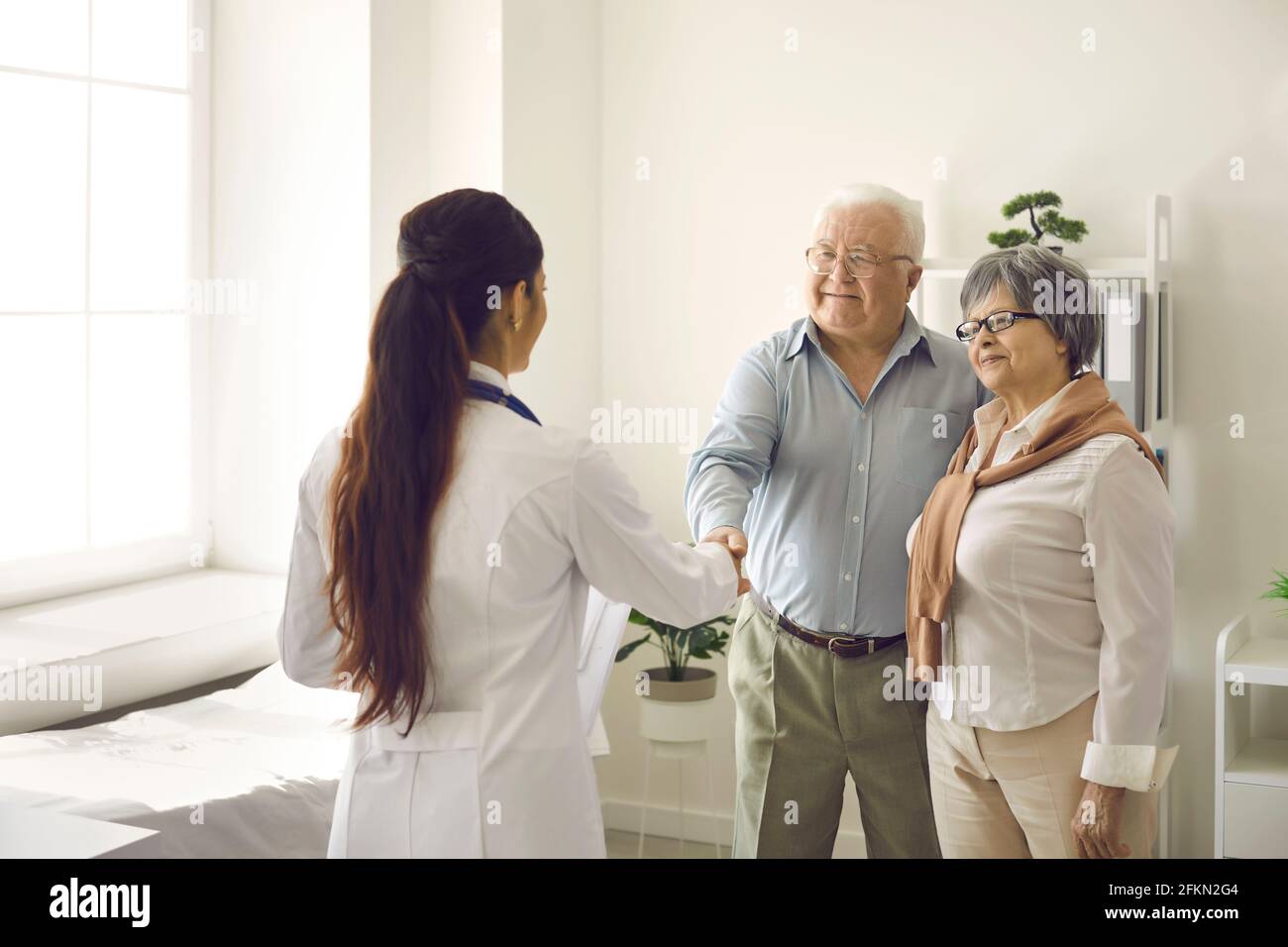 Glückliches Seniorenpaar, das sich bei einem Praktizierenden für die Hilfe und das Schütteln bedankte Hände mit ihr Stockfoto