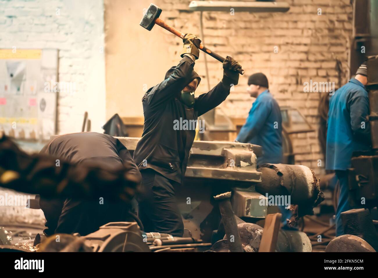 Arbeiter schwingt in einer metallverarbeitende Werkstatt einen Vorschlaghammer. Stockfoto
