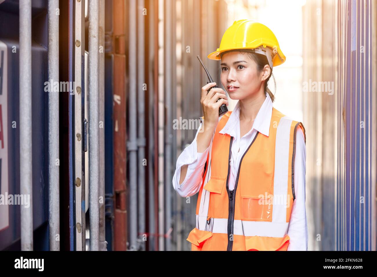 Portrait einer asiatischen Arbeiterin in Sicherheitsuniform im Gespräch mit Walkie Talkie zur Kontrolle der Arbeitsqualität im Containerlager. Arbeiten für Logistik und s Stockfoto