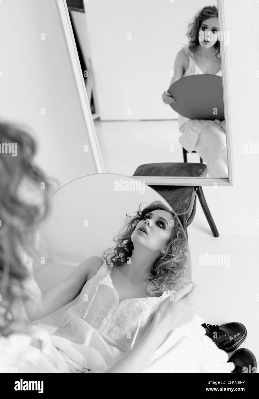 Portrait von attraktiven seltsam traurig Mädchen. Schöne neugierige junge Frau, die auf einem Stuhl am Spiegel mit Spiegel in den Händen sitzt. Schwarz und Weiß Stockfoto