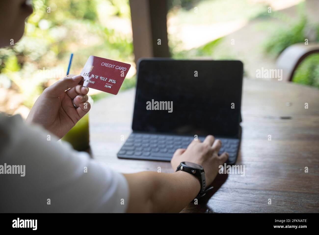 Asiatische Frau, die auf dem Boden am Sofa sitzt, mit einem Laptop online einkaufen und Kreditkartendaten für die Zahlung zu Hause eingeben. Stockfoto