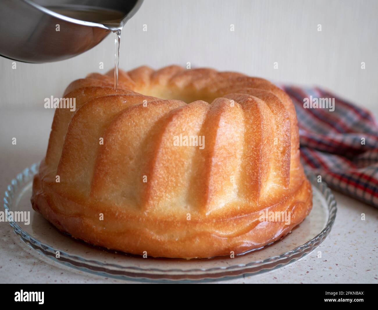 Frisch gebackener Rum baba. Den Sirup über den Savarin gießen. Rumpengetränkter Rundkuchen Stockfoto