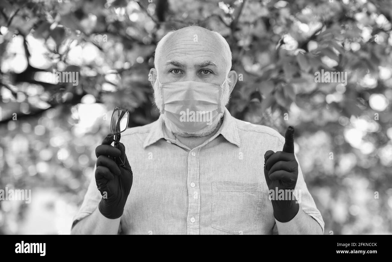 Befolgen Sie die Regeln. Senior Mann in medizinischen Maske und Handschuhe. sakura Baum im Park. Leben während Coronavirus Sperrung. Angst vor Krankheit. Strategie im Kampf Stockfoto