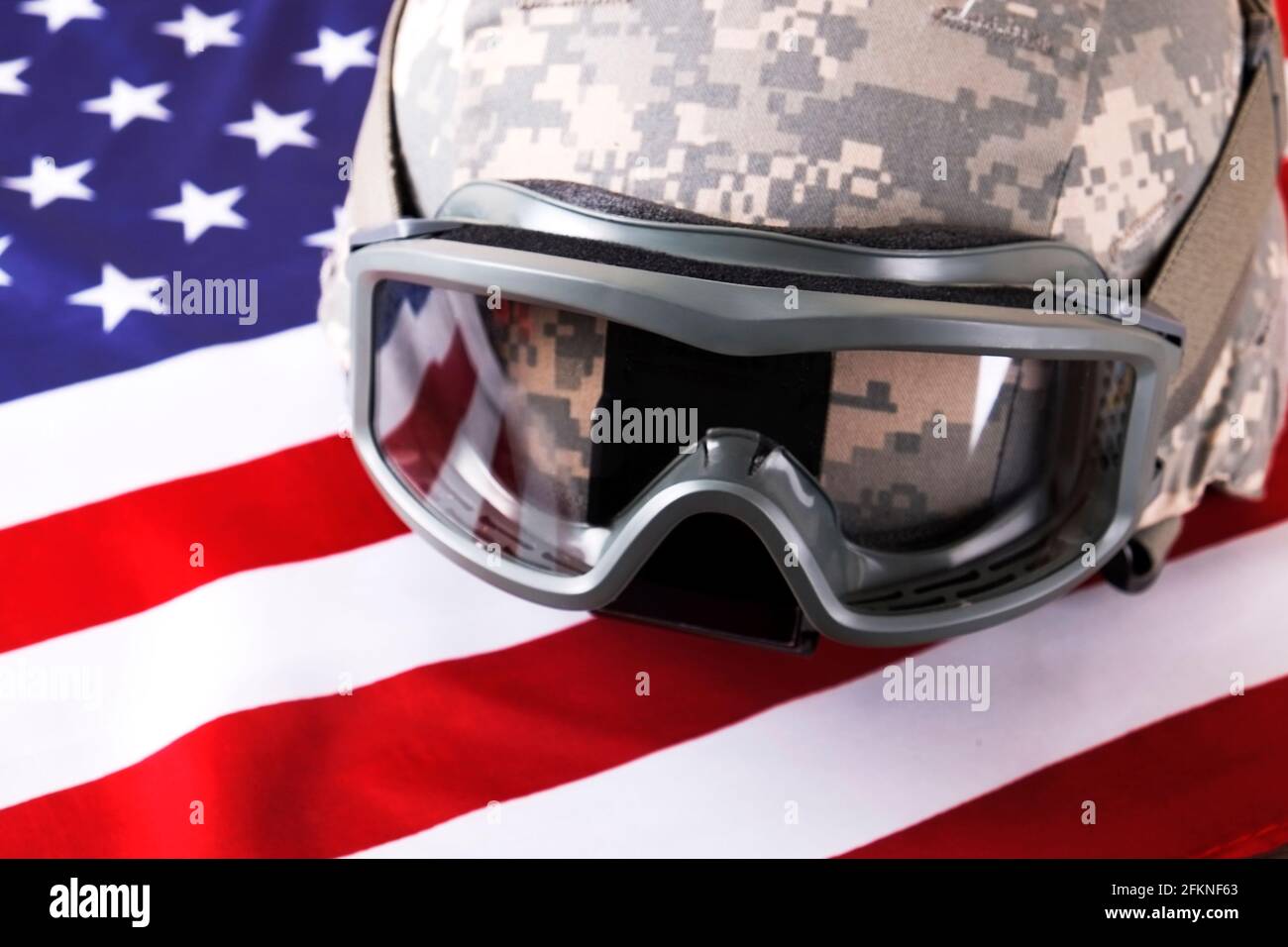 US Army Kevlar Kampfhelm, Camoabdeckung, taktische Brille, USA Flagge Hintergrund. Memorial Weekend, Veteranentag, United States of America Armed Forces Stockfoto