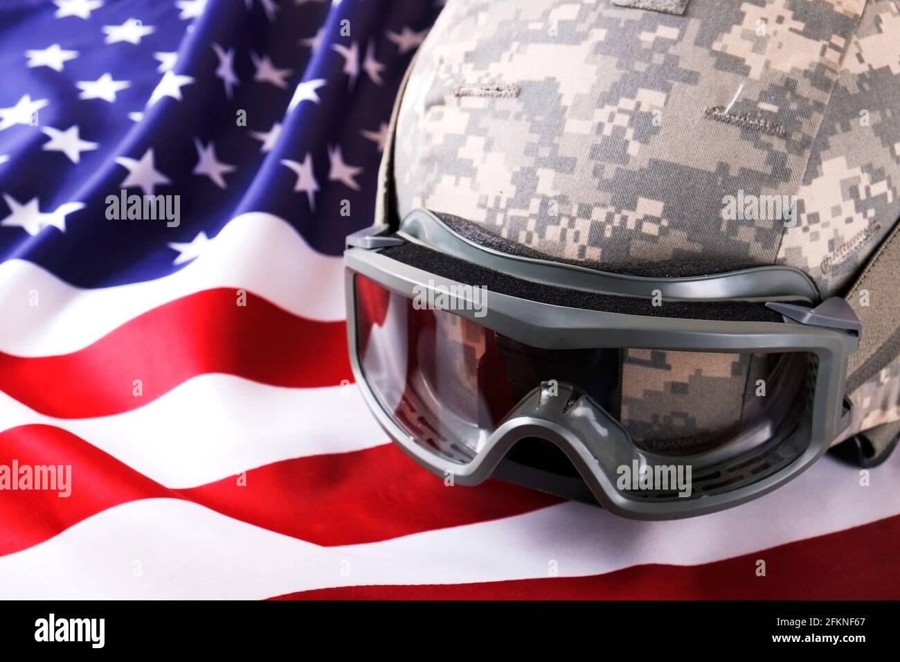 US Army Kevlar Kampfhelm, Camoabdeckung, taktische Brille, USA Flagge Hintergrund. Memorial Weekend, Veteranentag, United States of America Armed Forces Stockfoto