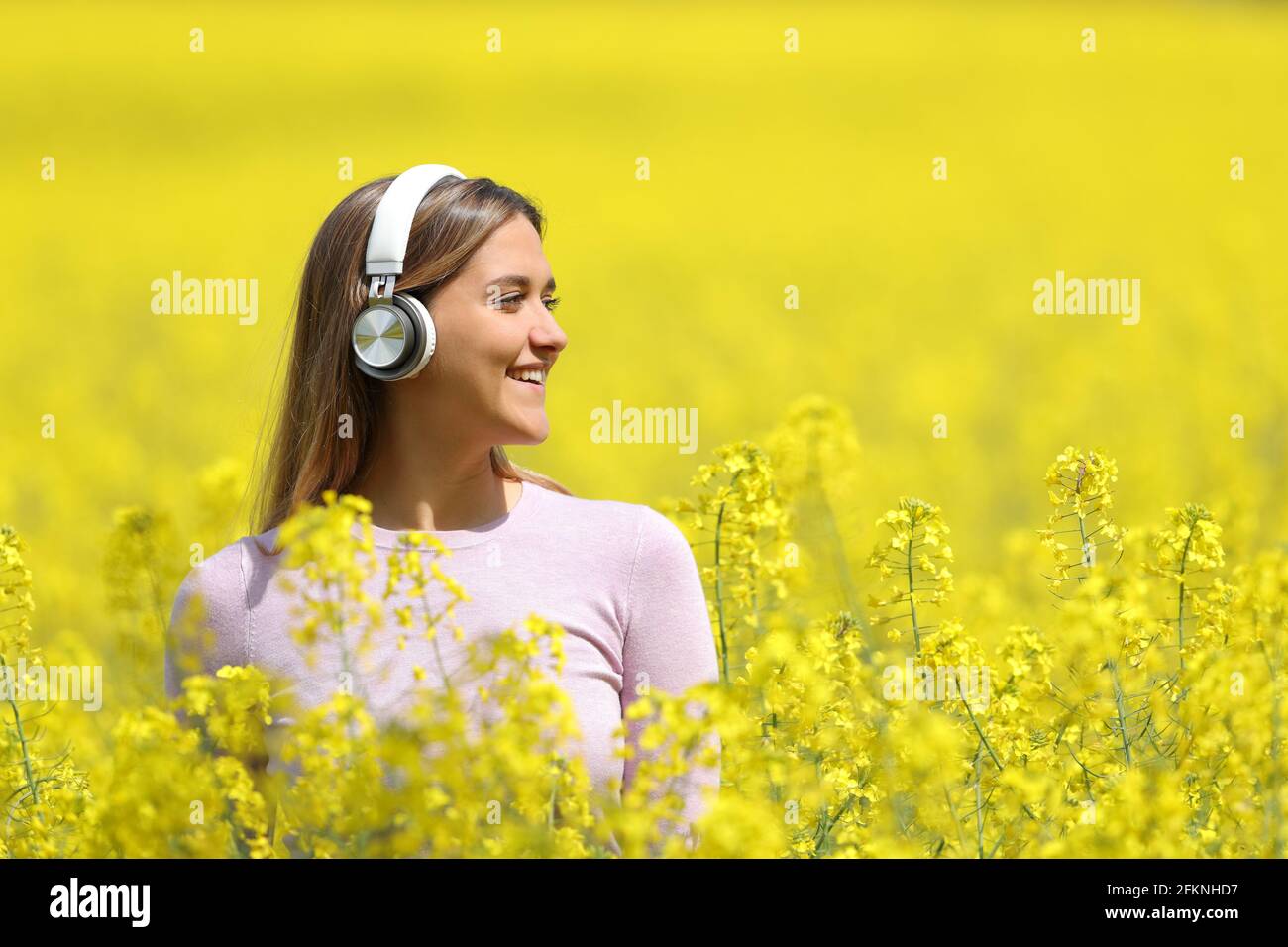 Fröhliche Frau, die mit Kopfhörern Musik hört und dabei die Blicke in sich zieht Ein gelbes Feld im Frühling Stockfoto