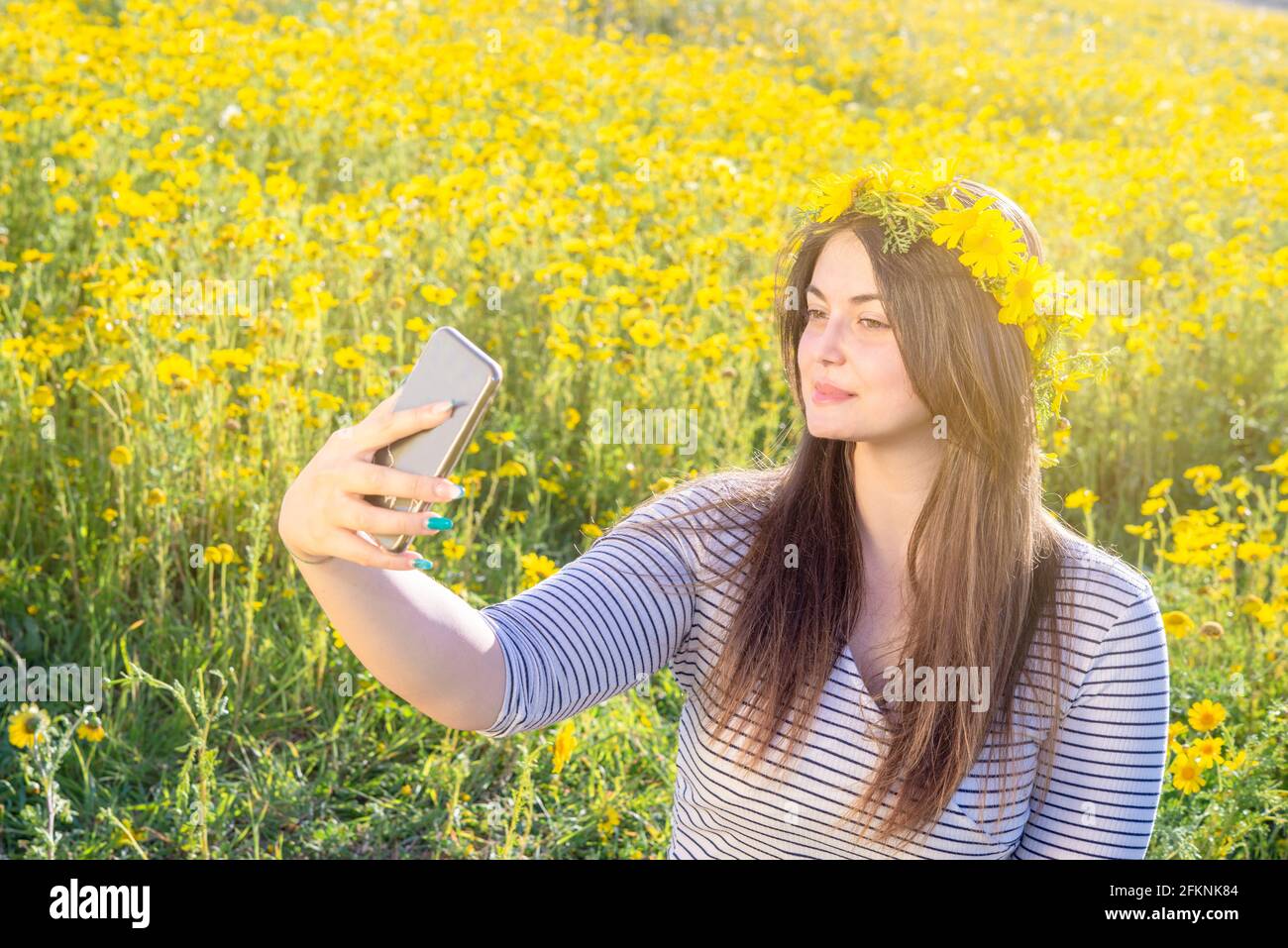 Schöne kurvige Frau posiert im Freien mit Gänseblümchen Krone. Machen Sie Selfie auf einer Wiese mit Gänseblümchen Stockfoto
