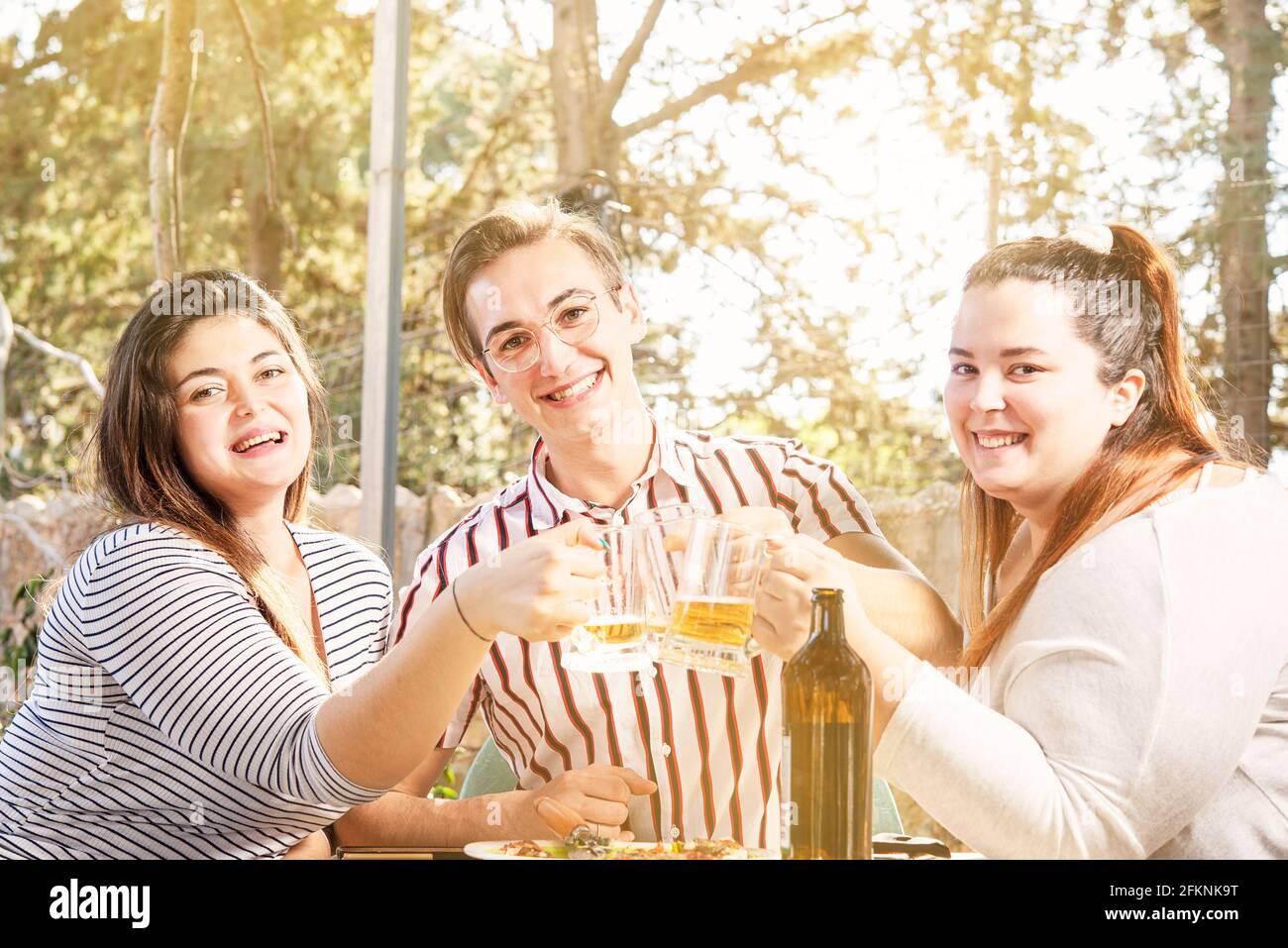 Drei Freunde, Mann und Frau, feiern lächelnd an der Bar Toasten mit Bierkrügen Stockfoto