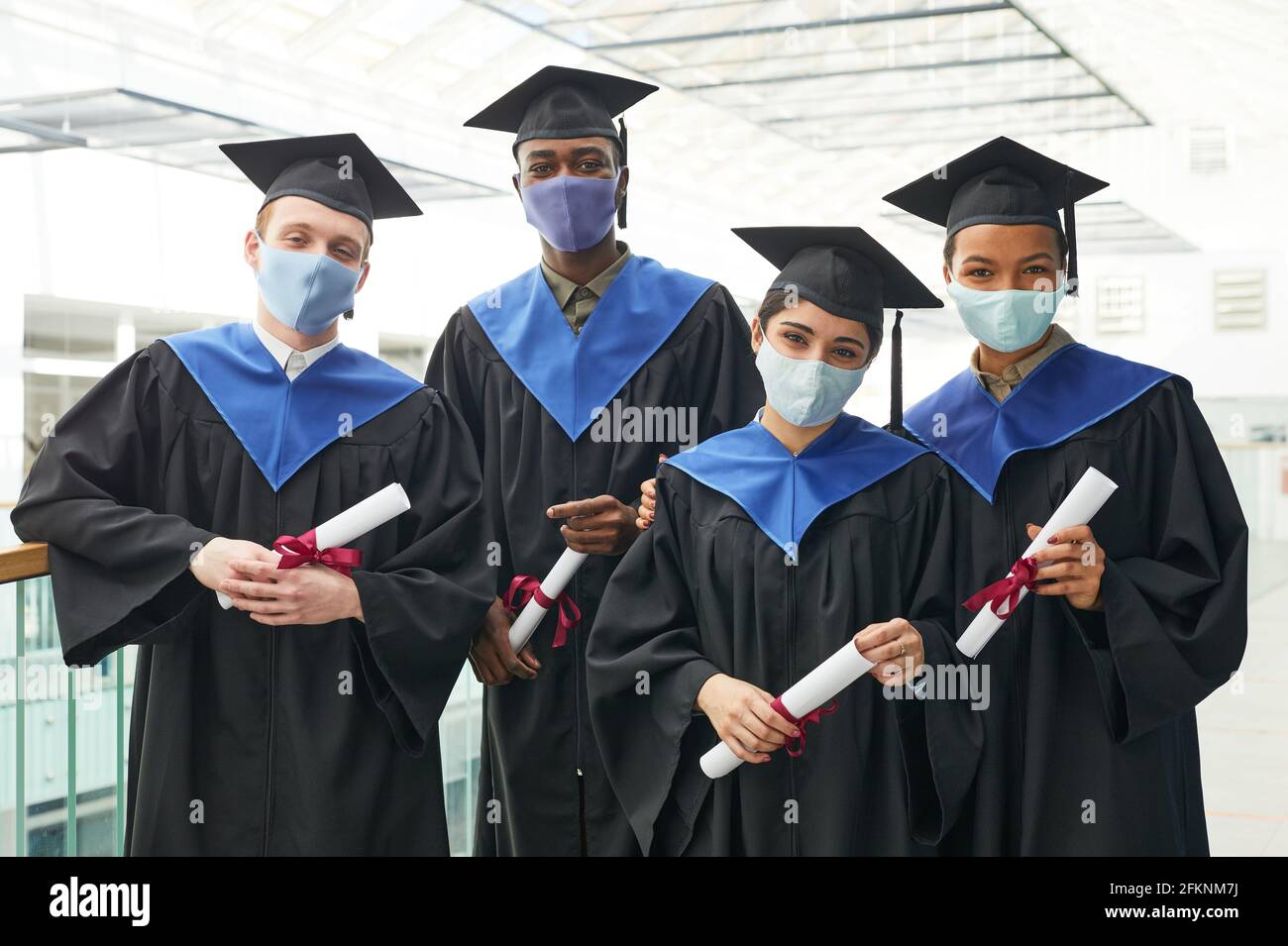 Eine vielfältige Gruppe junger Menschen, die Abschlusskleider und Masken tragen Beim Posen drinnen im College-Interieur Stockfoto