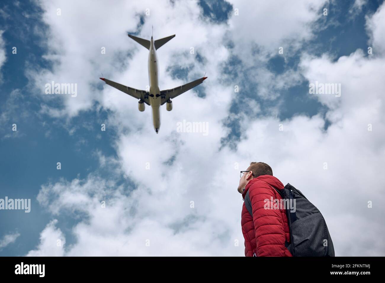 Junger Mann, der auf ein fliegendes Flugzeug gegen den wolkigen Himmel blickt. Themen Nostalgie für Reisen und Luftfahrt. Stockfoto