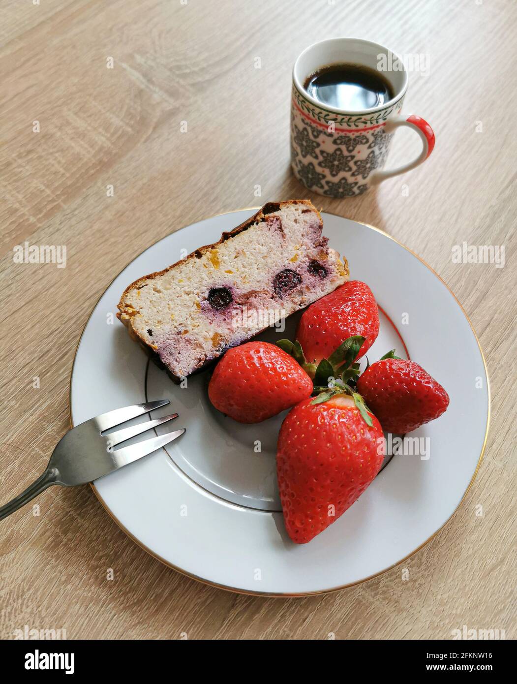 Ein Stück hausgemachter Käsekuchen mit Heidelbeeren, Erdbeeren auf einem weißen Teller und Kaffee Stockfoto