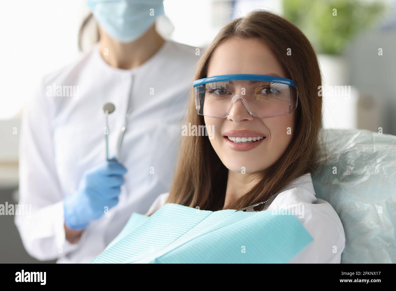 Frau Patientin in einer Sicherheitsbrille, die in einem Zahnarztstuhl in der Nähe sitzt Arzt Stockfoto Frau Patientin in einer Sicherheitsbrille, die in einem Zahnarztstuhl in der Nähe sitzt Arzt Stockfoto