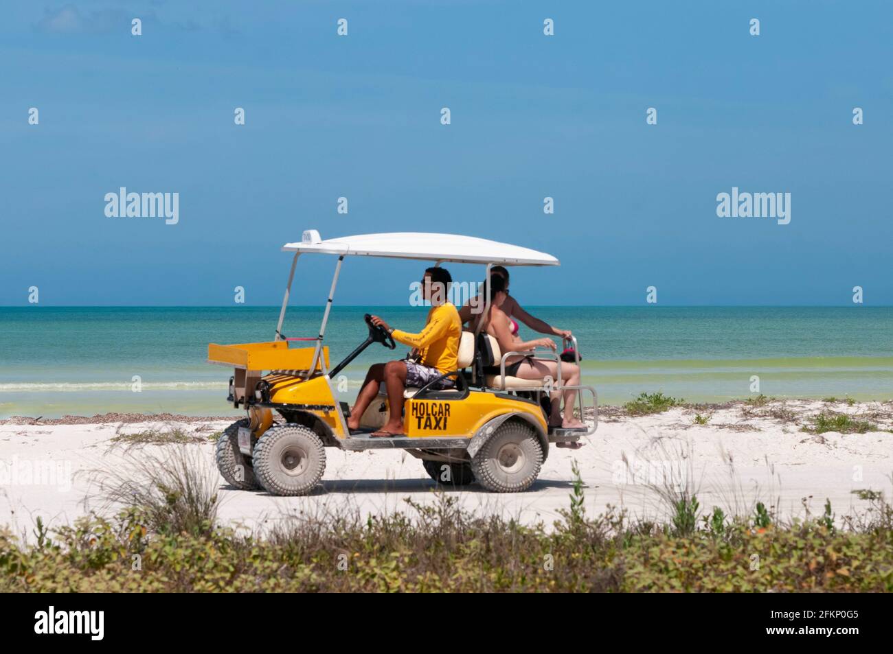 Ein gelbes Golfauto-Taxi an einem tropischen Strand auf der Insel Holbox in Mexiko, das Touristen trägt. Im Hintergrund des Karibischen Meeres und des Blues Stockfoto