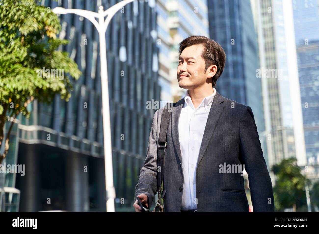 asiatischer Geschäftsmann, der im zentralen Geschäftsviertel in zu Fuß arbeitet Moderne Stadt Stockfoto