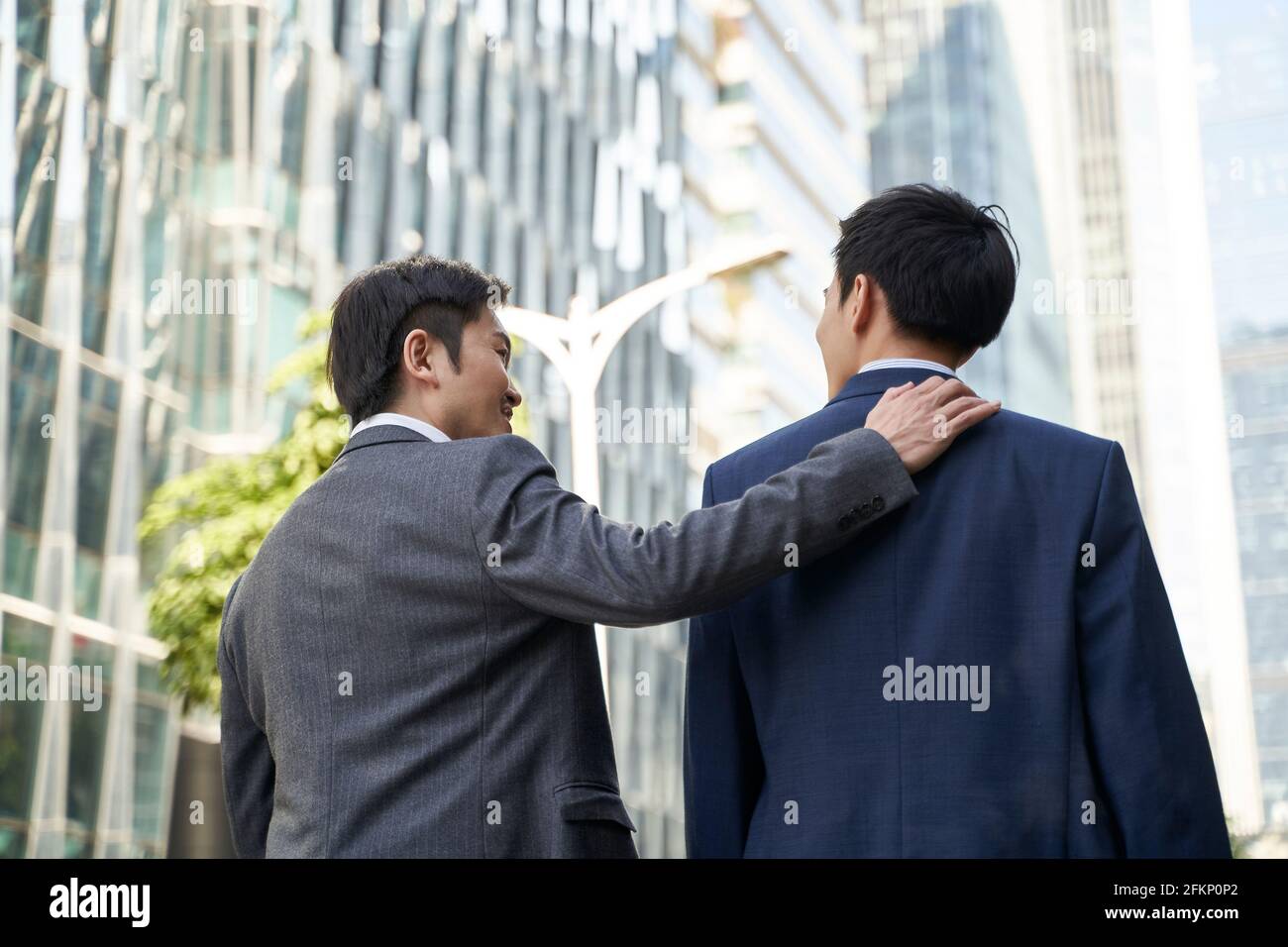 die asiatische Unternehmensleitung gibt dem Untergebenen einen Kumper auf den Rücken Während Sie in der Straße des zentralen Geschäftsviertels der Moderne zu Fuß Stadt Stockfoto