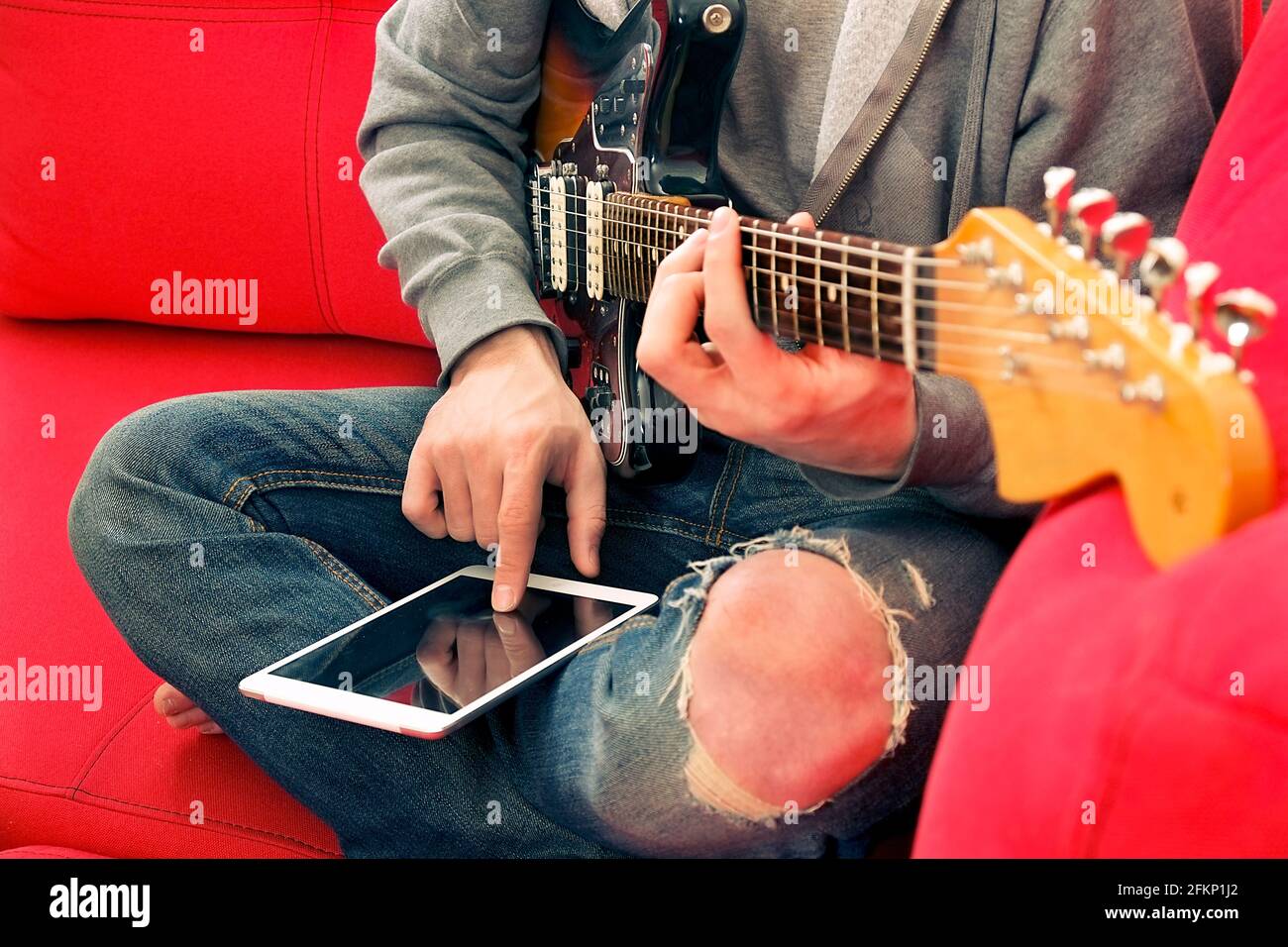 Lässiger junger Mann in zerrissenen Jeans, spielt Sunburst-Offset-E-Gitarre.  Junger Musiker, der Online-Musikinstrumentenkurs auf Wireless i nimmt  Stockfotografie - Alamy