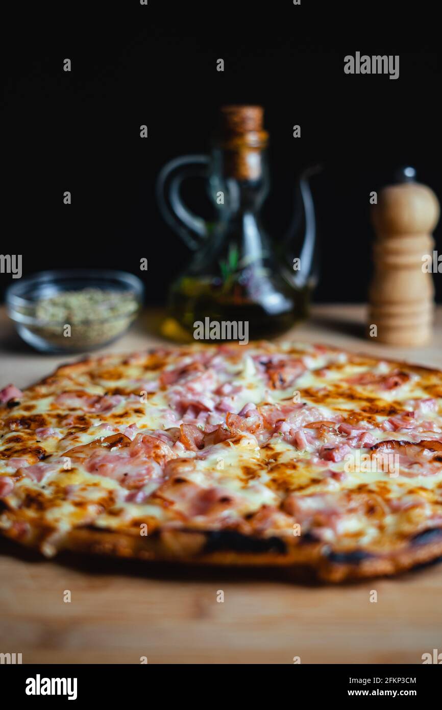 Eine Pizza auf einem Holztisch. Im Hintergrund stehen der Orangeano, das Olivenöl und der Pfeffer. Stockfoto
