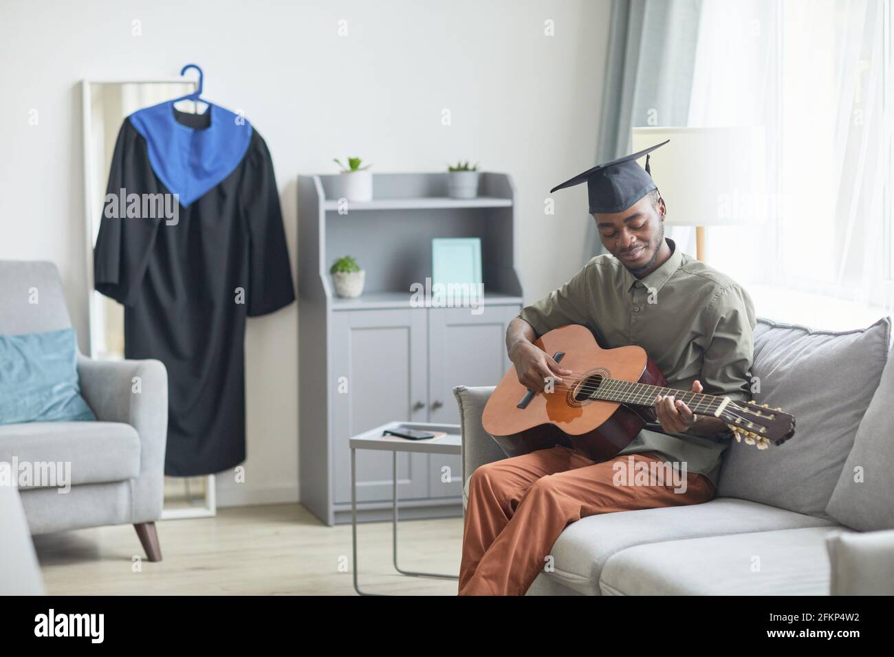 Porträt eines jungen afroamerikanischen Mannes, der zu Hause Gitarre spielt Vorbereitung auf die Abschlussfeier Stockfoto