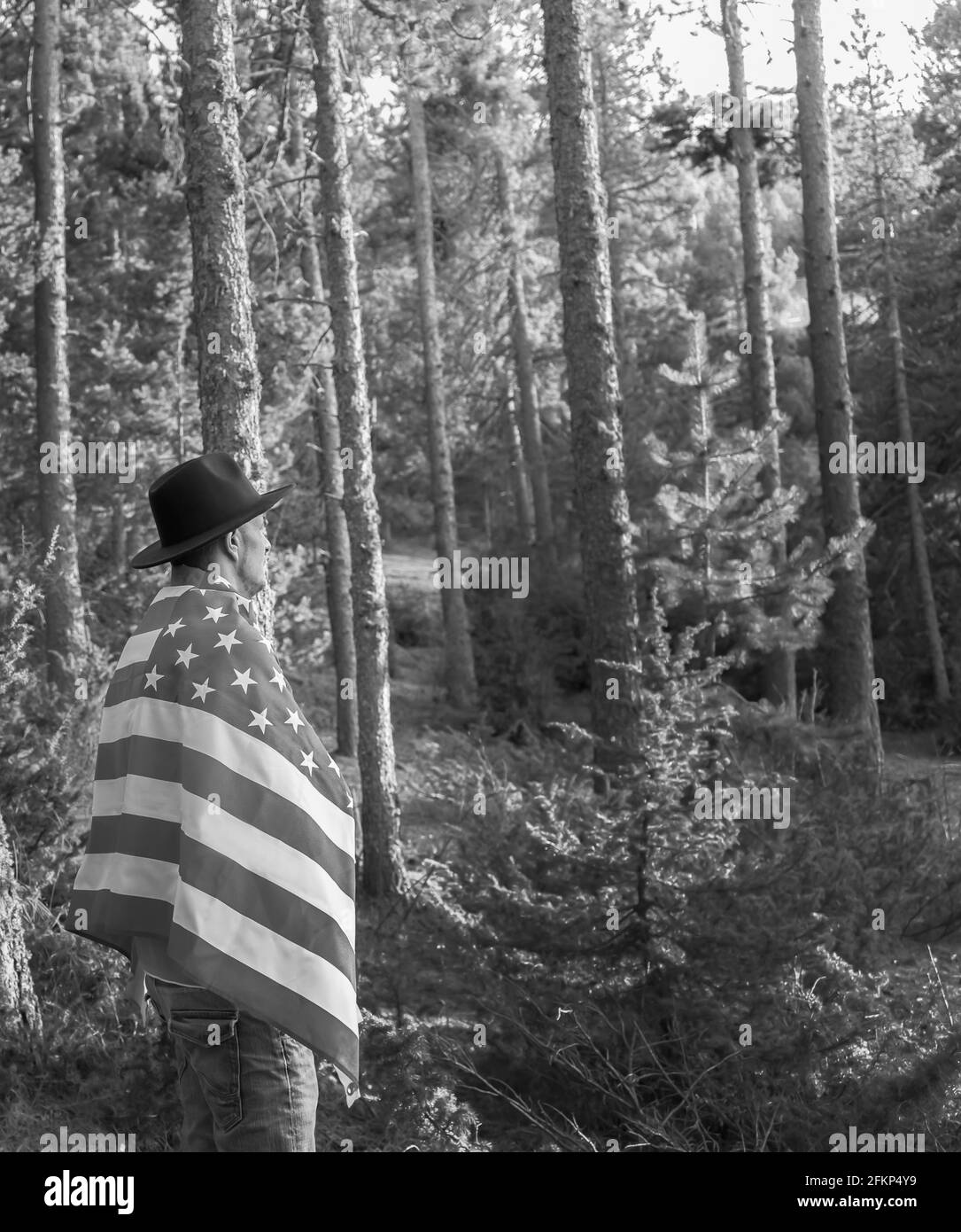 United States Independence Day Feier Konzept, 4. Juli.Mann in schwarzem Cowboy-Hut mit amerikanischer Flagge im Waldpark.Schwarz-Weiß-Stil Stockfoto