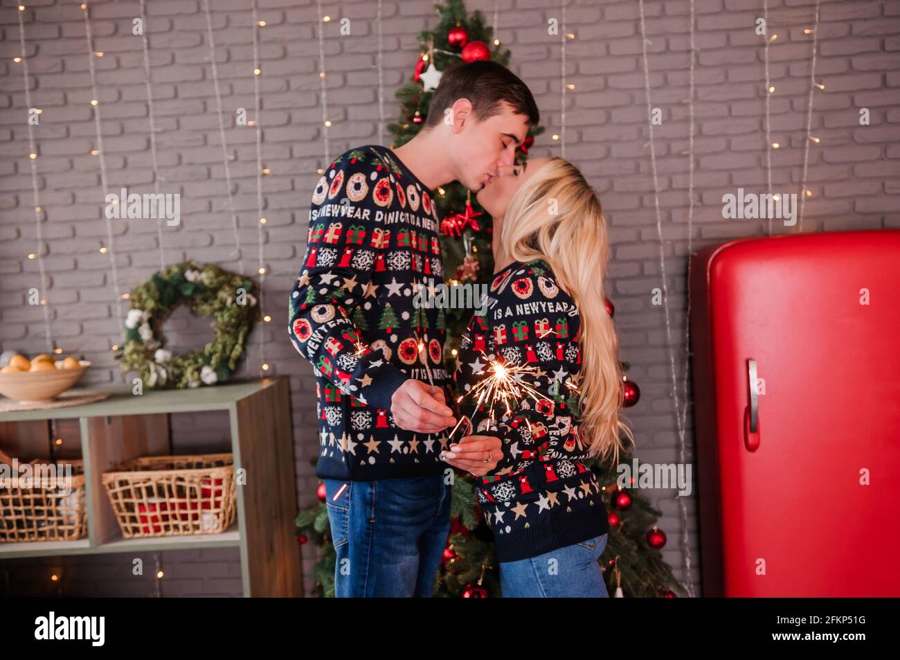 Ein Kerl mit einem Mädchen in einem Pullover und Jeans umarmen, küssen und halten Wunderkerzen in den Händen Stockfoto