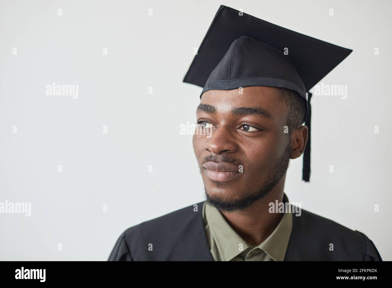 Kopf- und Schulterporträt eines selbstbewussten afroamerikanischen Mannes mit Graduierung hut gegen Weiß Stockfoto