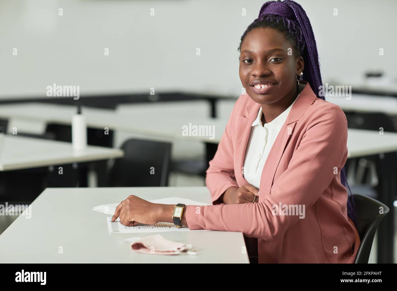Minimalporträt einer jungen afroamerikanischen Frau, die in der Schule lächelt, während sie im Klassenzimmer am Schreibtisch sitzt und Platz kopiert Stockfoto