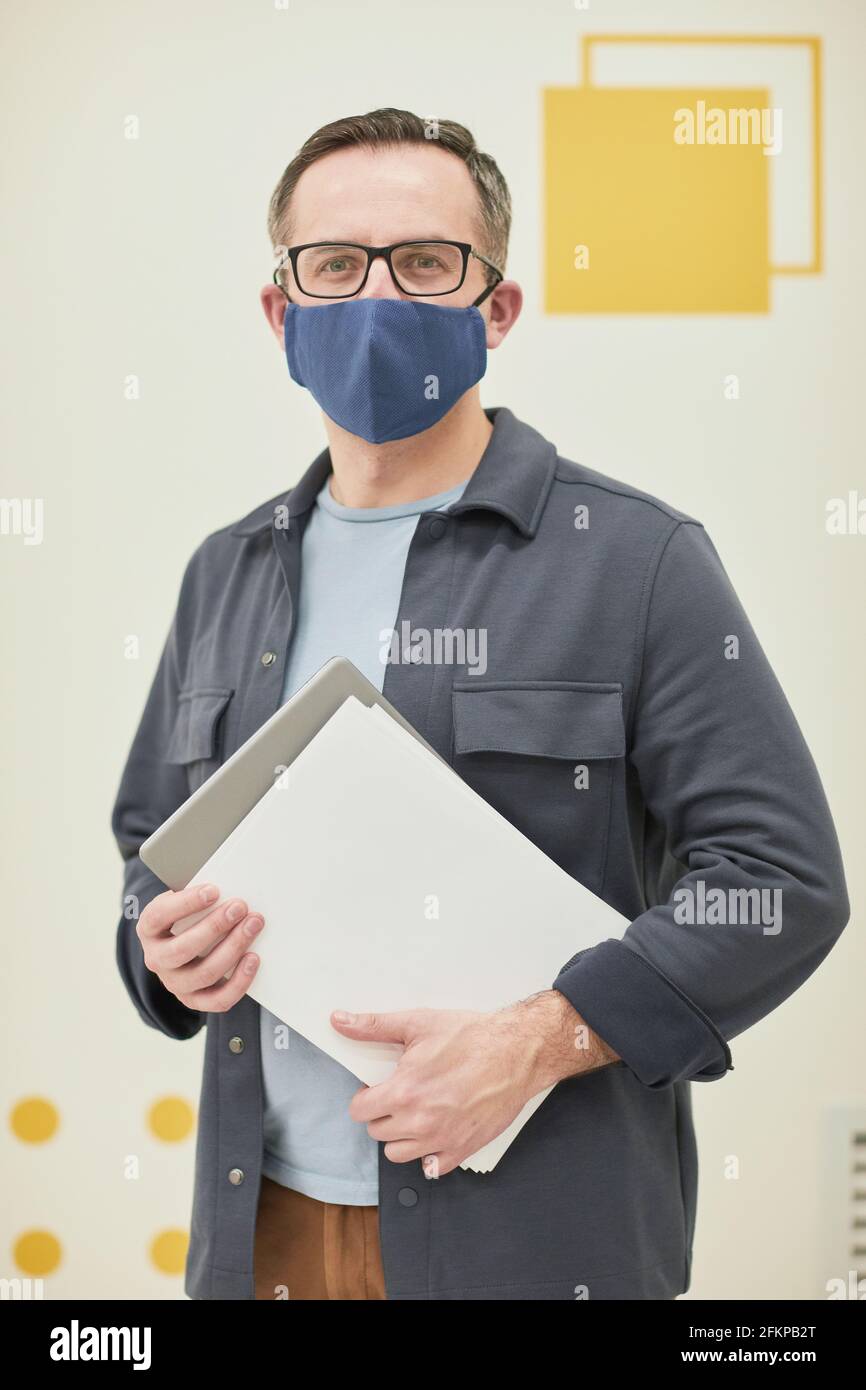Vertikales Porträt eines reifen männlichen Lehrers, der in der Schule eine Maske trägt Im Klassenzimmer und mit Blick auf die Kamera Stockfoto