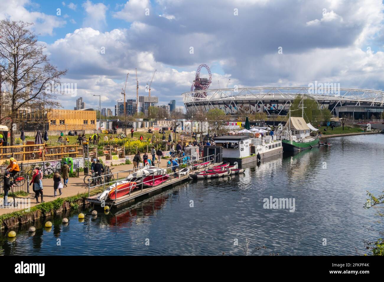 LONDON, Großbritannien - 11. APRIL 2021: Menschen vor den Grachtenbars in Hackney Wick in London an einem sonnigen Tag. Im Hintergrund sieht man das West Ham Stadium. Stockfoto