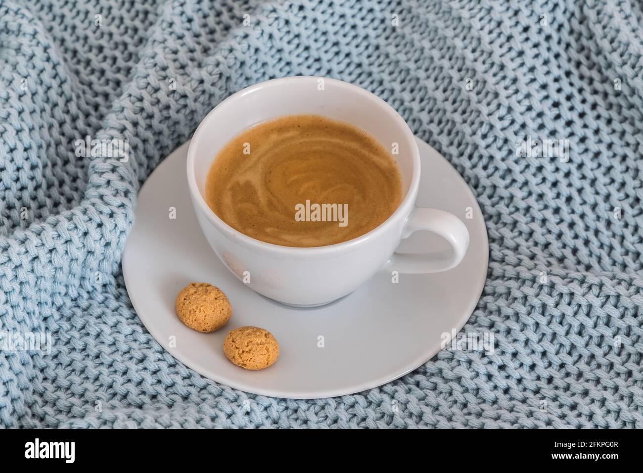 Tasse Kaffee auf einer hellblauen Strickdecke aus Wolle. Gemütliche Atmosphäre. Kaffeepause, zu Hause bleiben Konzept. Stockfoto