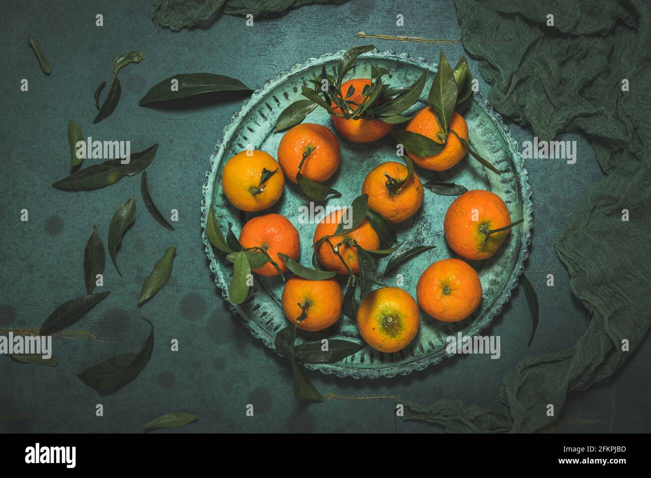 Mandarinen mit Blättern auf grüner Platte auf grünem Hintergrund, Draufsicht Stockfoto