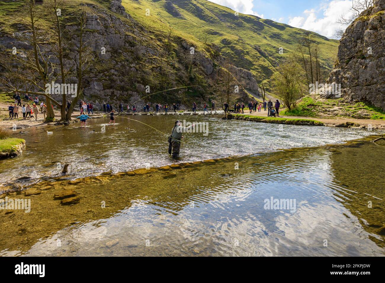 Dovedale Stepping Stones, Peak District, Derbyshire, Großbritannien. Menschen, die den Fluss überqueren. Fischer im Fluss Angeln. Stockfoto