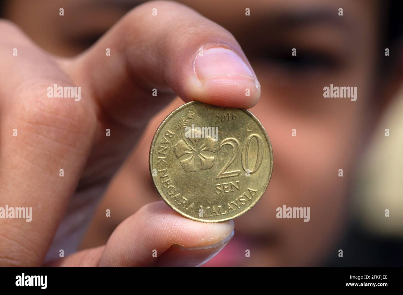 Asiatische Kinderhand mit einer 20-sen-Ringgit-Malaysia-Münze, ausgewähltem Fokus und verschwommenem Hintergrund Stockfoto
