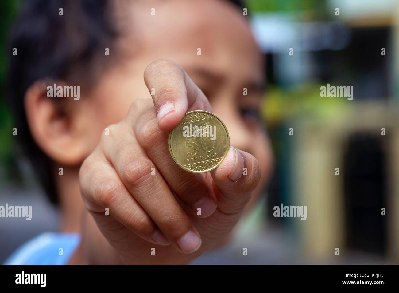 Asiatische Kinderhand mit einer Fifty Halalas Riyal-Münze, Saudi-Arabien-Geld, ausgewählter Fokus Stockfoto